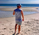 Man standing on a beach wearing a 'Thirsty Threads Australia' muscle tee and Thirsty Threads hybrid striped boardshorts
