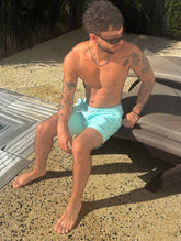 Man sitting by a pool wearing Thirsty Threads Aqua hybrid boardshorts.