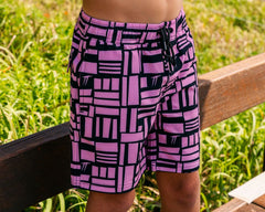 Child wearing Thirsty Threads boys pink geometric anti-chafe hybrid boardshorts at the entrance to the beach