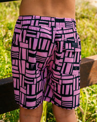 Child wearing Thirsty Threads boys pink geo anti-chafe hybrid boardshorts at the beach entrance - back view