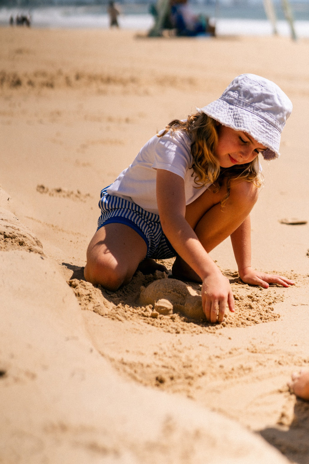 Girl playing in the sand wearing Thirsty Threads Azure Stripe girls' hybrid boardshorts with a soft built-in liner