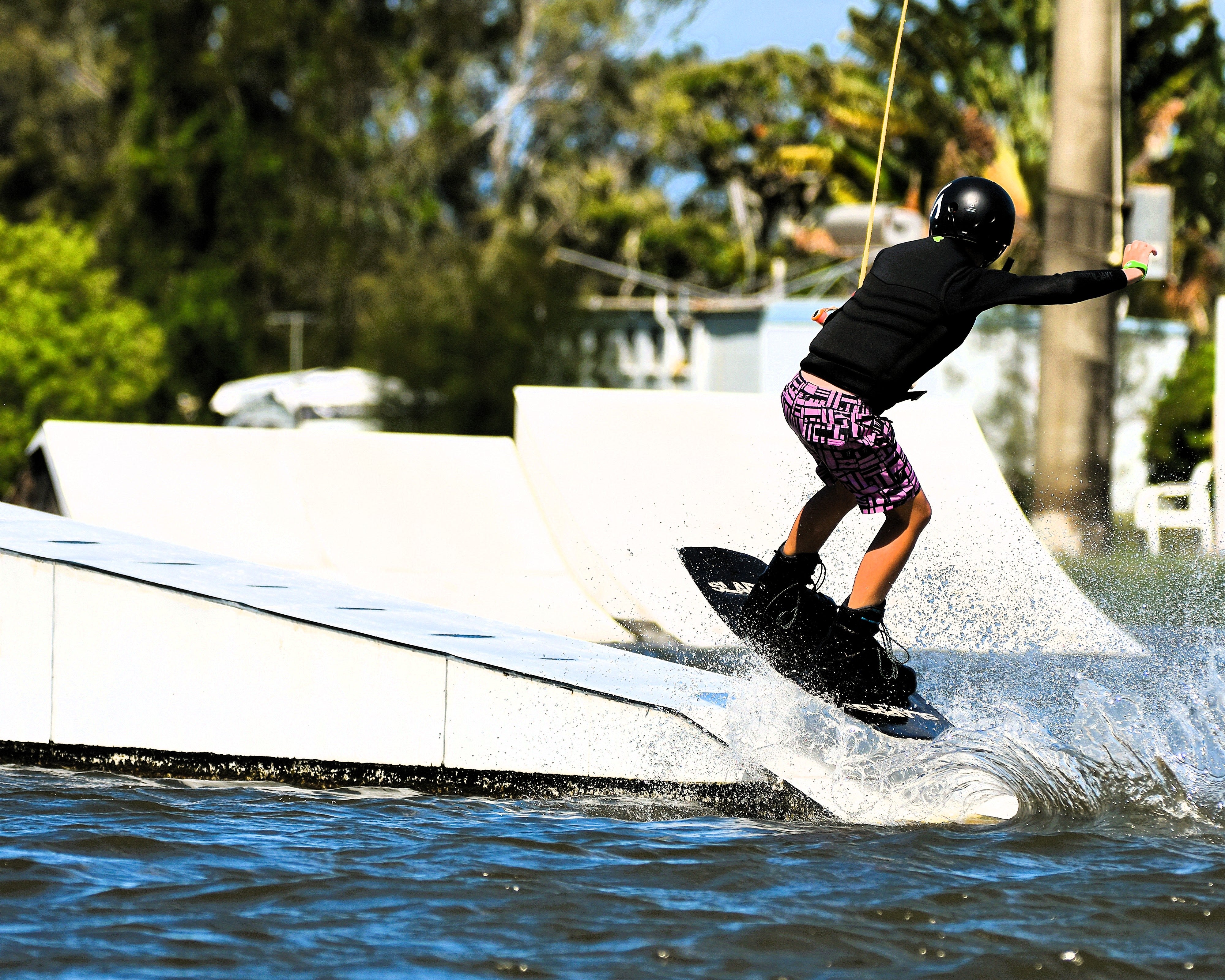 A wakeboarder wearing Thirsty Threads Pink Geo Hybrid Boardshortsdoing a 50-50 trick at a wake park