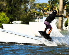 A wakeboarder wearing Thirsty Threads Pink Geo Hybrid Boardshortsdoing a 50-50 trick at a wake park
